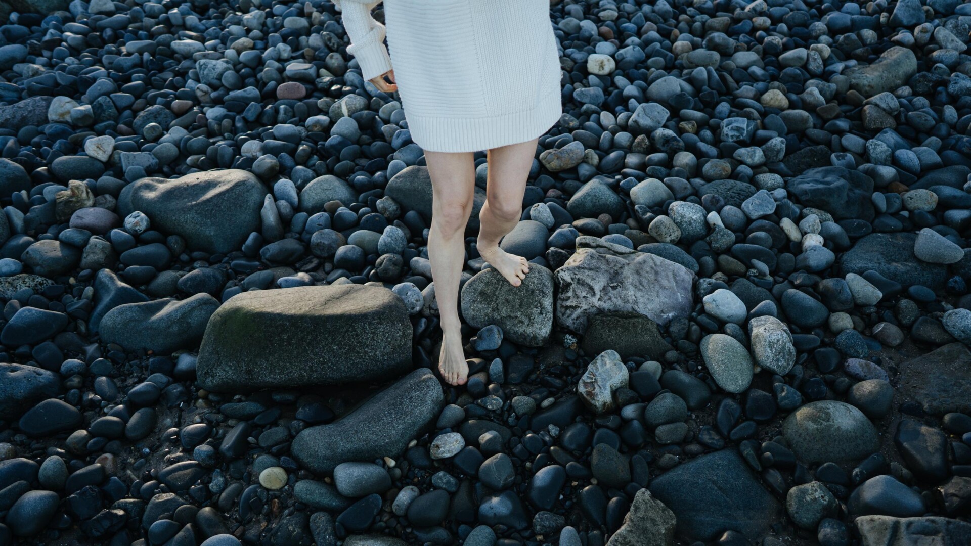 Women in a white dress walks over black stones