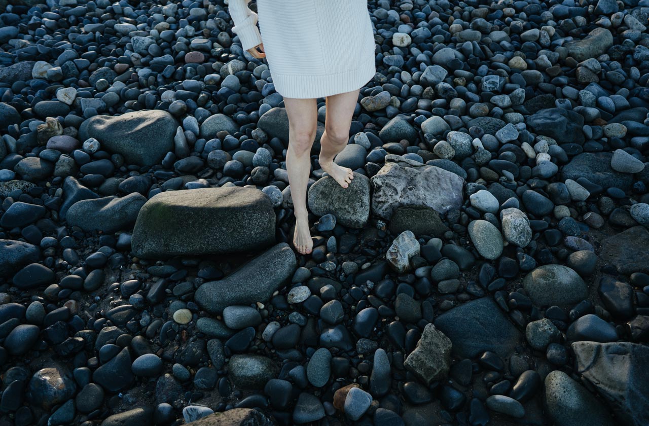 Frau in weissem Kleid geht übe dunkle Steine